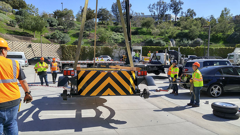 The TrafFix Devices shipping crew loading Scorpion Towable Attenuators onto a flatbed semi-trailer using a crane
